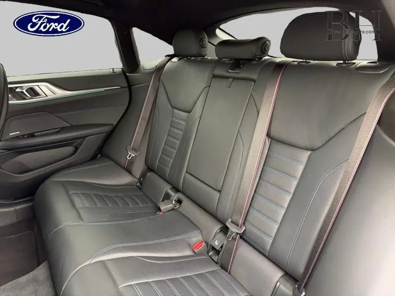 Vue intérieure arrière de la BMW Série 4 Gran Coupe 420iA 2022, sièges cuir noir avec surpiqûres bleues et ceintures rouges.