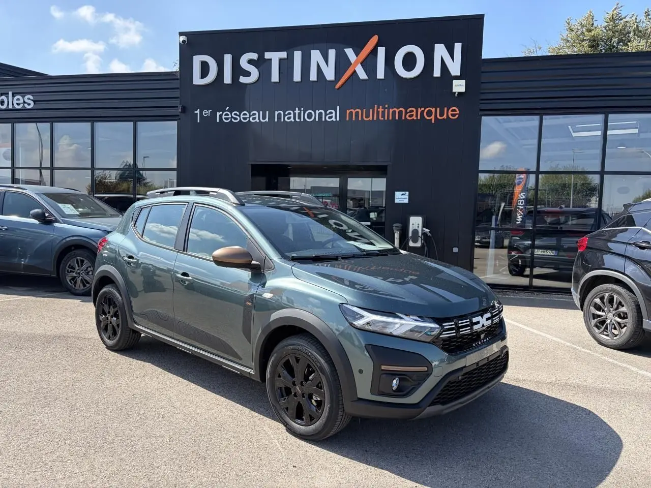 Vue 3/4 avant gauche d'une Dacia Sandero III Stepway 2025 vert cèdre avec jantes noires et coques de rétroviseur cuivrées.