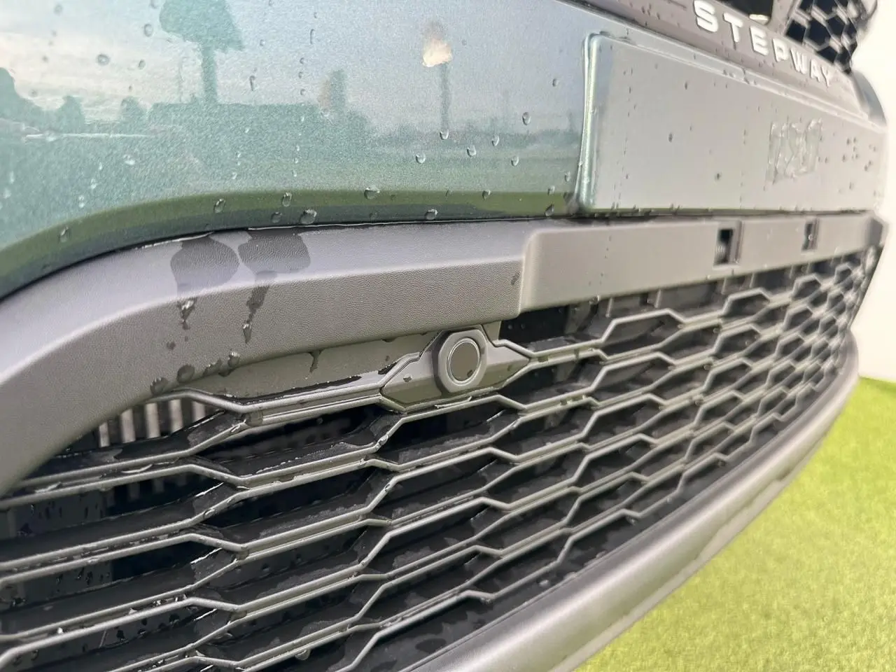 Gros plan sur la calandre noire et le bouclier avant du Dacia Sandero III Stepway vert cèdre avec capteur de stationnement.