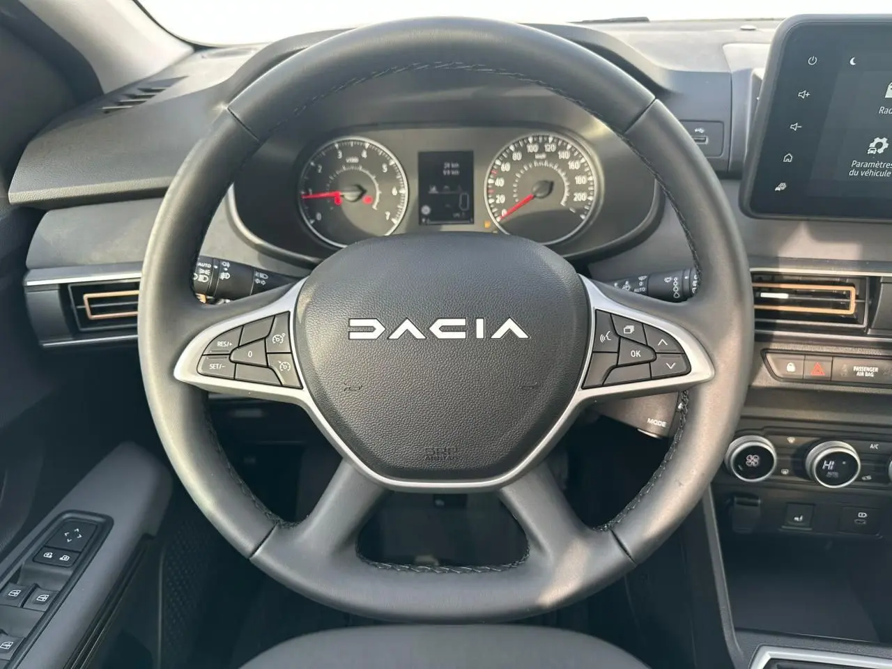 Vue intérieure centrée sur le volant noir avec logo Dacia, tableau de bord analogique et écran tactile à droite.