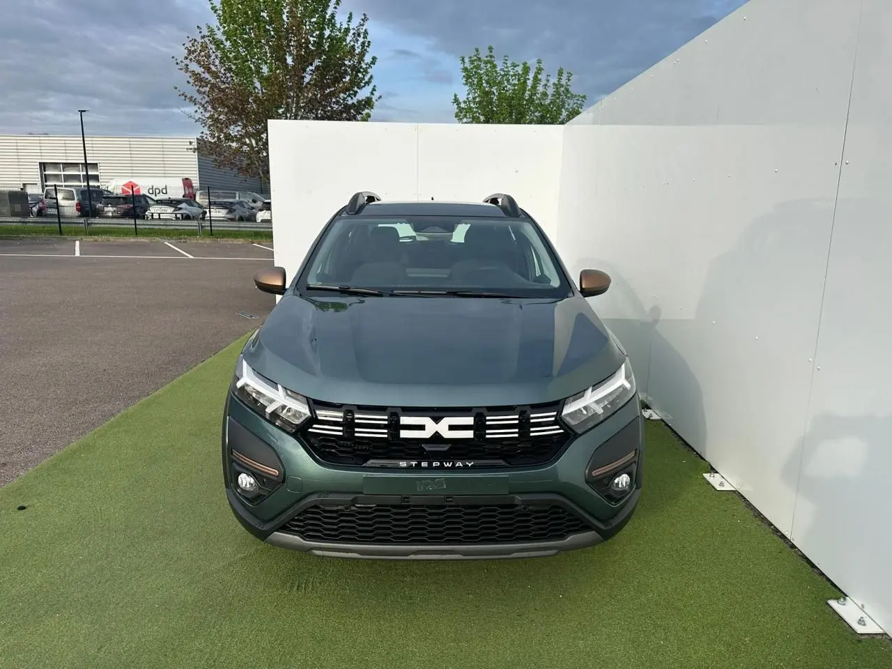 Vue avant d'une Dacia Sandero III Stepway vert cèdre avec calandre noire et détails brun cuivré sur pare-chocs et rétroviseurs.