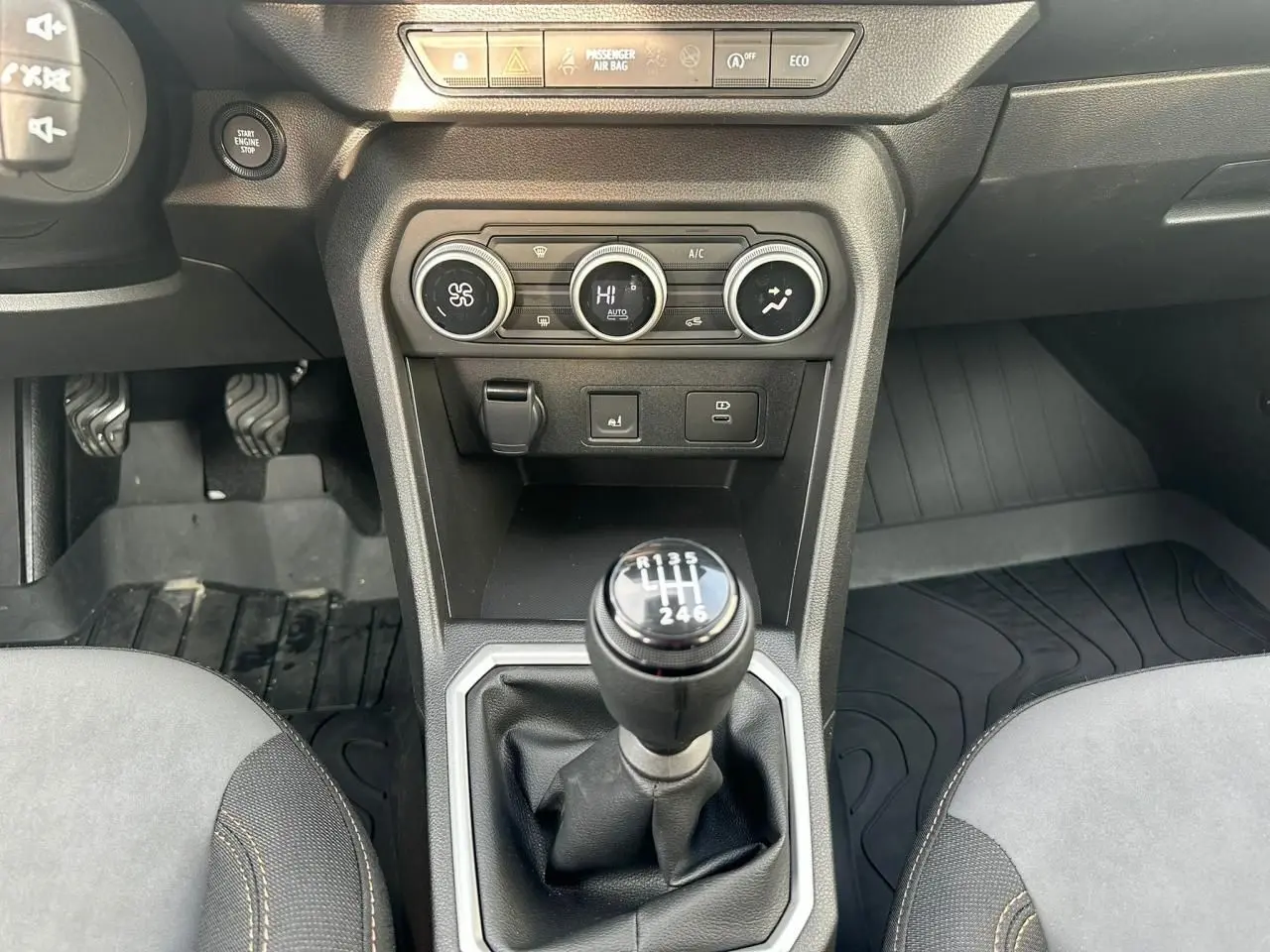 Vue intérieure centrée sur le levier de vitesses manuel de la Dacia Sandero III Stepway, avec commandes climatisation et pédales visibles.