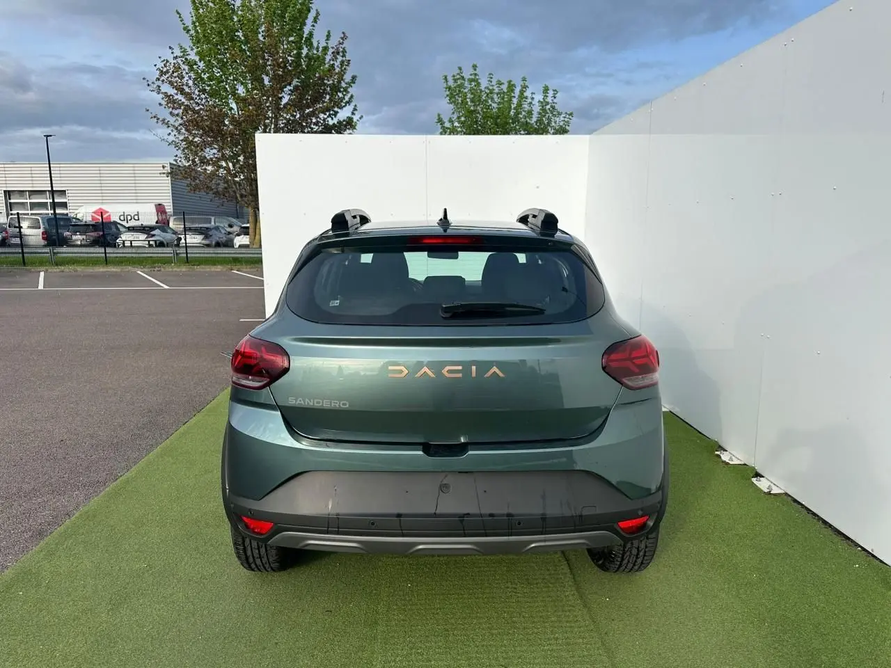 Vue arrière d'une Dacia Sandero III Stepway vert cèdre avec logo et lettrage brun cuivré, sur fond urbain.