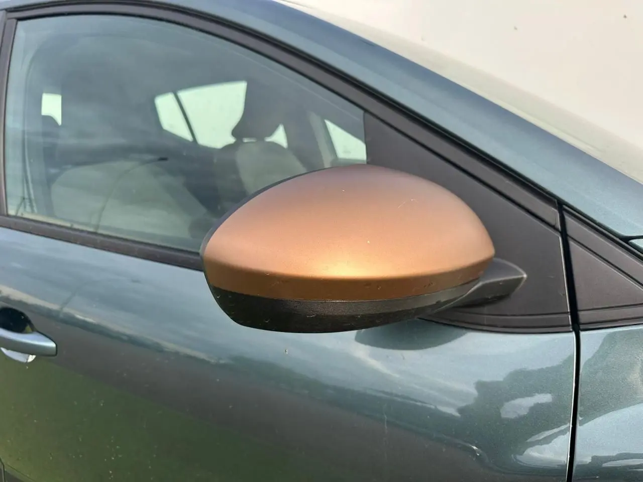 Gros plan sur le rétroviseur droit brun cuivré d'une Dacia Sandero III Stepway vert cèdre, côté conducteur visible.