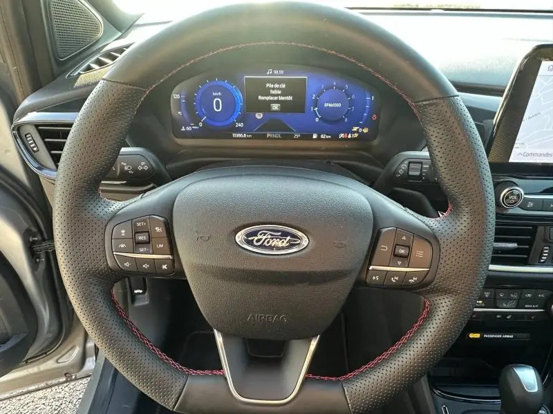 Vue centrée sur le volant en cuir perforé avec surpiqûres rouges du Ford Puma 2024, tableau de bord numérique en arrière-plan.