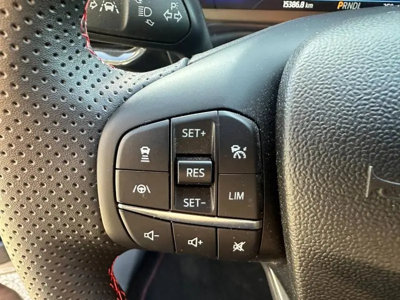 Gros plan sur les commandes de régulateur et limiteur de vitesse au volant perforé noir du Ford Puma gris Solar Métallisée 2024.