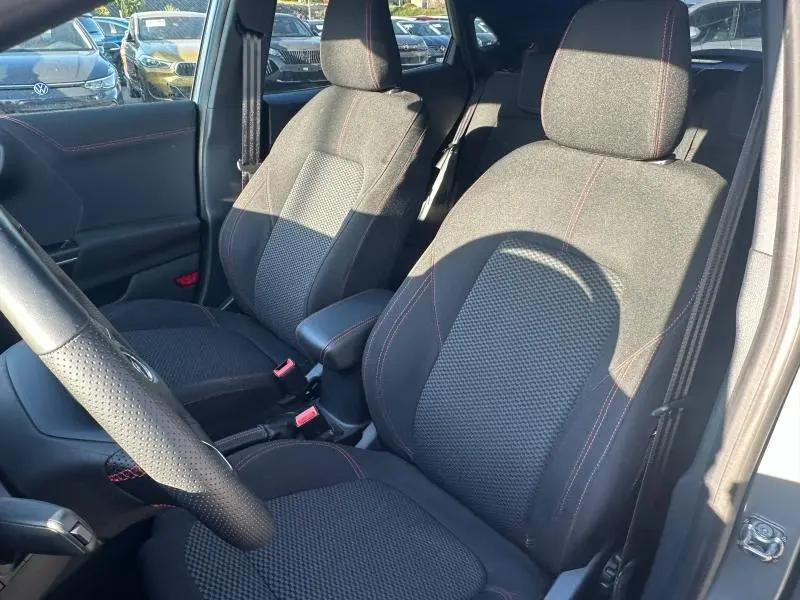 Vue intérieure côté avant droit du Ford Puma 2024, sièges noirs avec surpiqûres rouges et volant en cuir perforé.