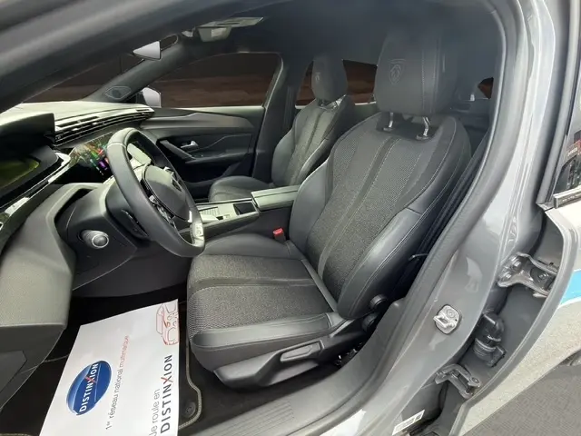 Vue intérieure côté conducteur du Peugeot 408 Hybrid gris clair, sièges en cuir et tissu avec logo Peugeot brodé sur les appuie-têtes.