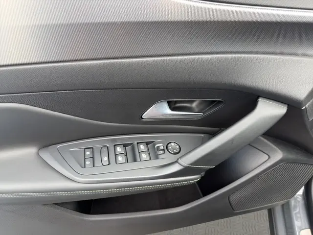 Gros plan sur la porte côté conducteur du Peugeot 408 Hybrid gris clair, montrant les commandes électriques des vitres et la poignée intérieure.