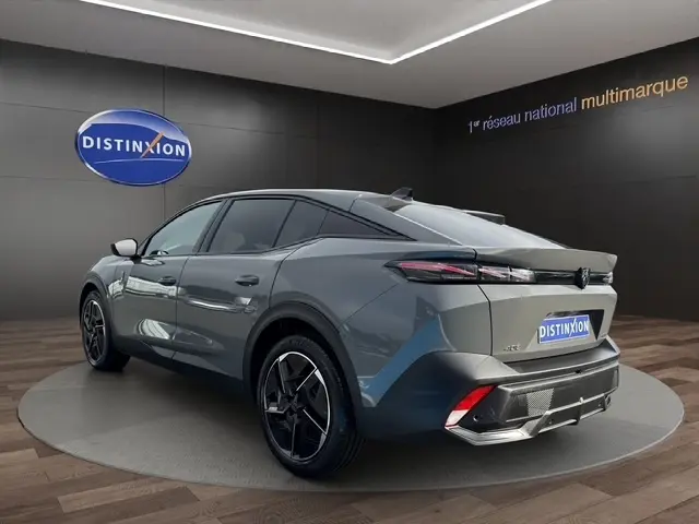 Vue 3/4 arrière droite d'une Peugeot 408 Hybrid gris clair avec jantes noires et feux arrière LED, en intérieur showroom.