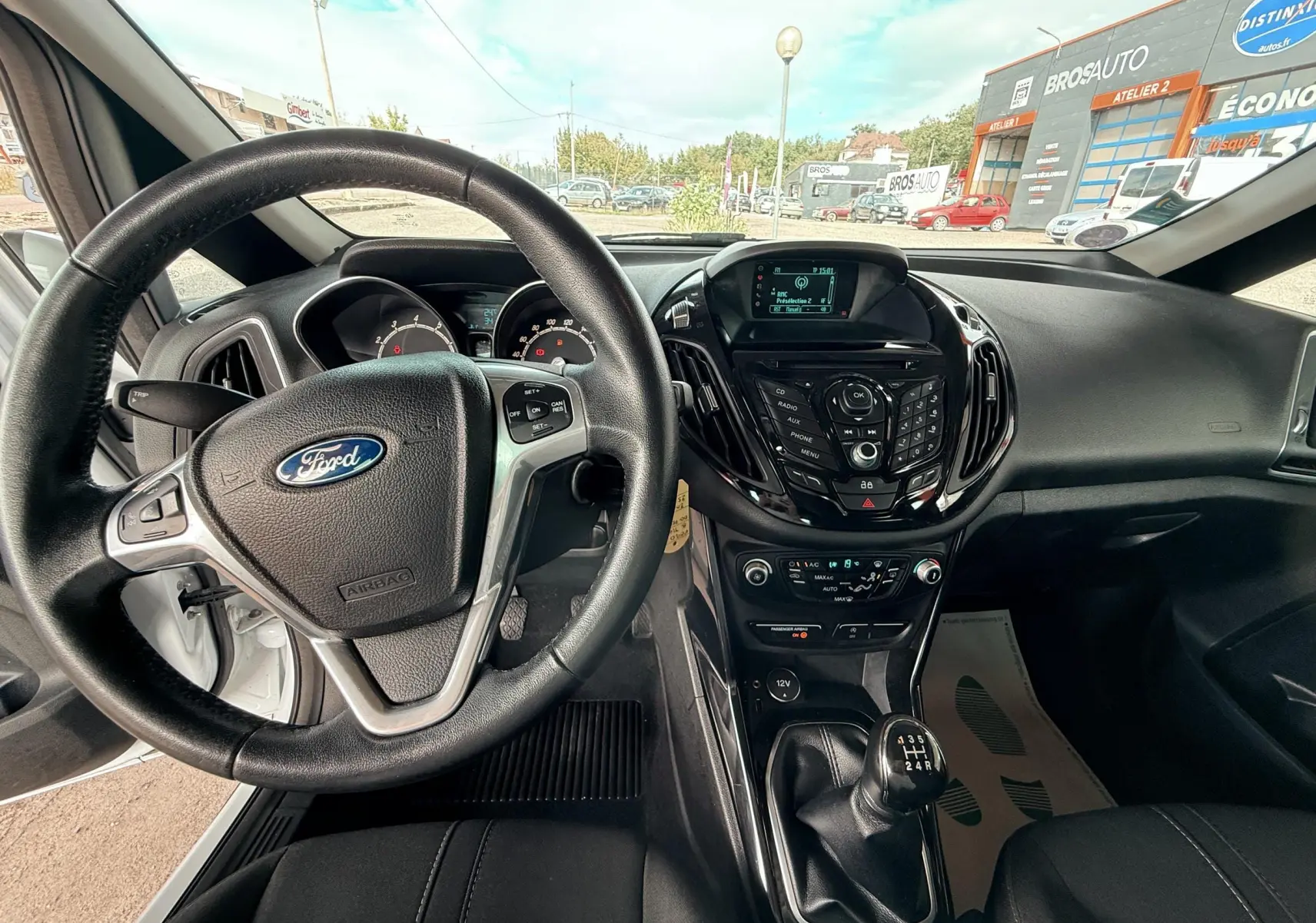 Vue intérieure du poste de conduite d'une Ford B-MAX blanche de 2014, volant et levier de vitesses manuelle visibles.