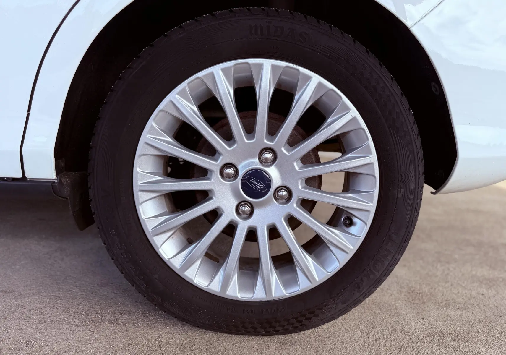 Gros plan sur la roue avant gauche d'une Ford B-MAX blanche avec jante alliage argentée et logo Ford central.