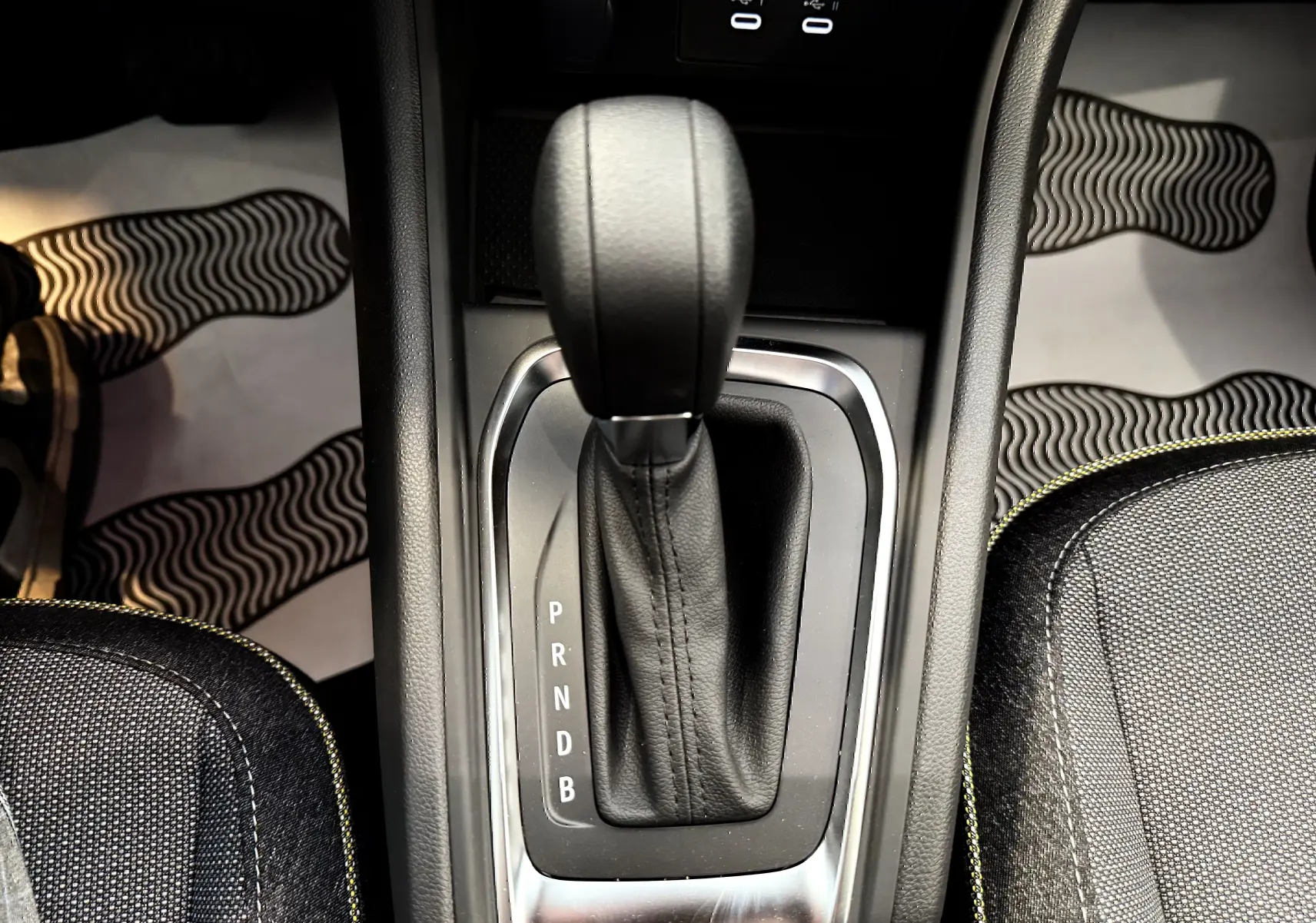 Le levier de vitesses automatique noir du Renault Captur 2025 hybride, entouré de garnitures grises et sièges tissu avec surpiqûres jaunes.