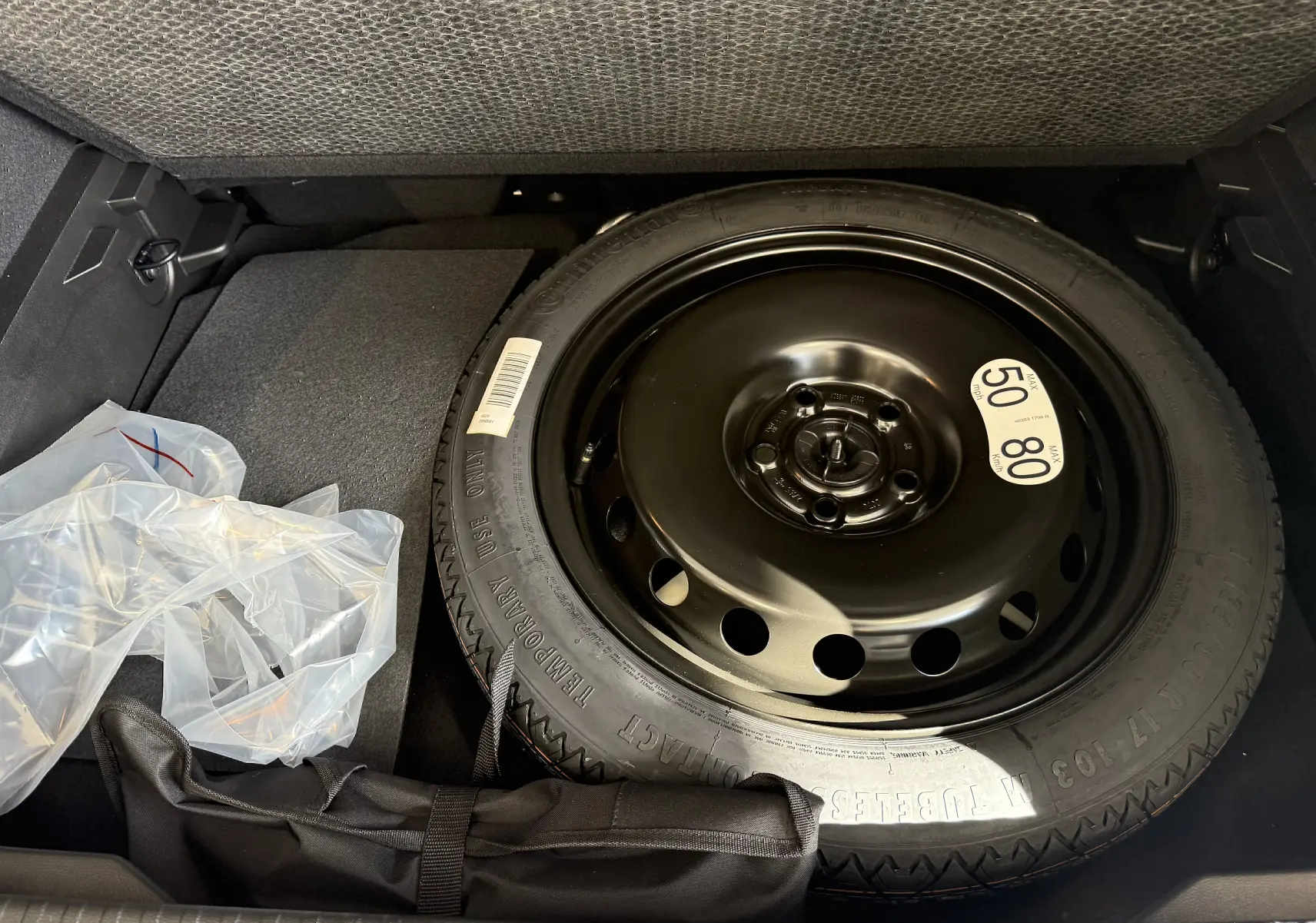 Vue plongeante sur la roue de secours noire dans le coffre du Renault Captur gris Cassiopée 2025 avec accessoires rangés à côté.