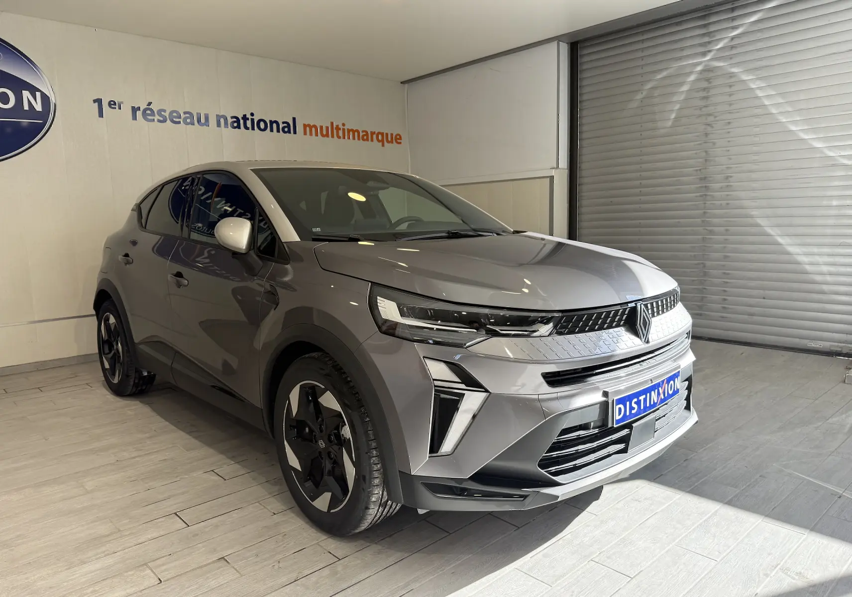 Renault Captur 2025 gris Cassiopée métal avec toit gris, vue 3/4 avant droit dans un showroom lumineux.