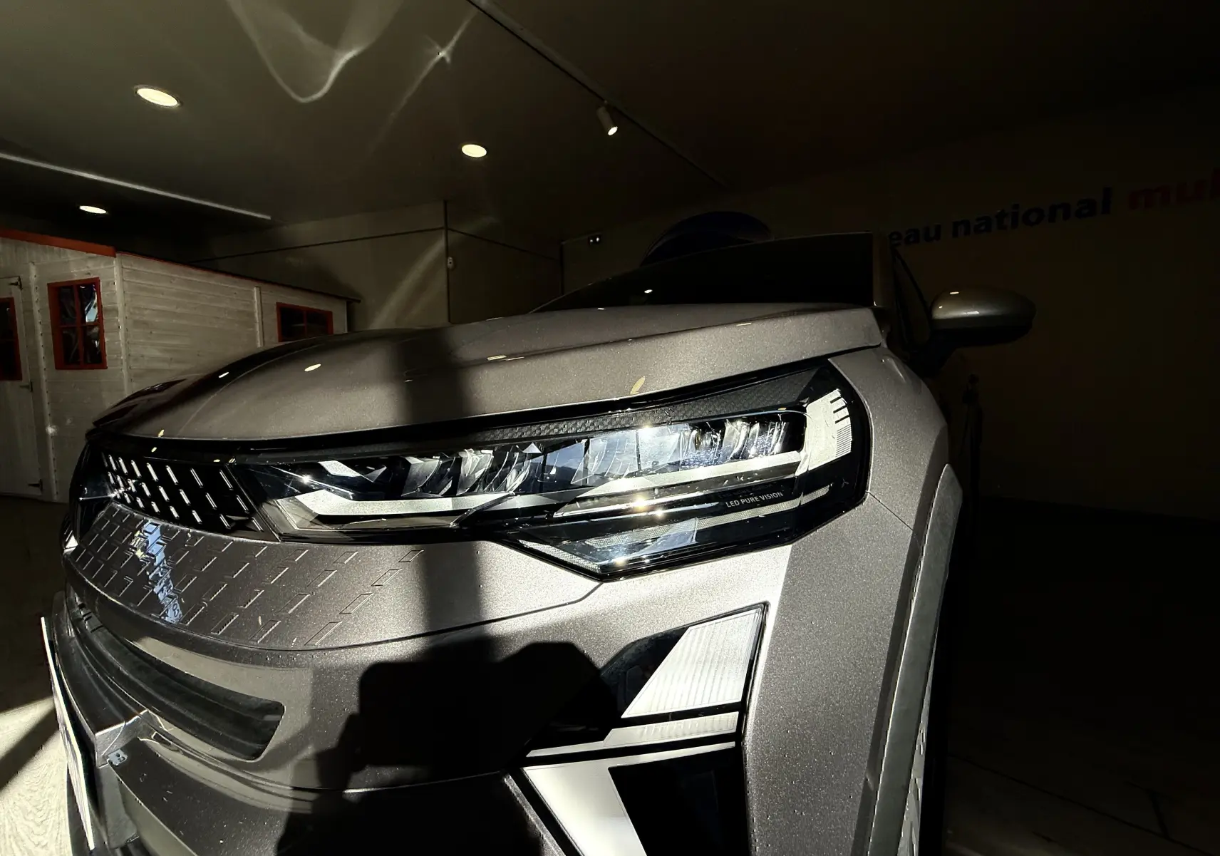 Gros plan sur l'avant droit du Renault Captur gris Cassiopée métal, mettant en valeur le phare LED et la calandre texturée.