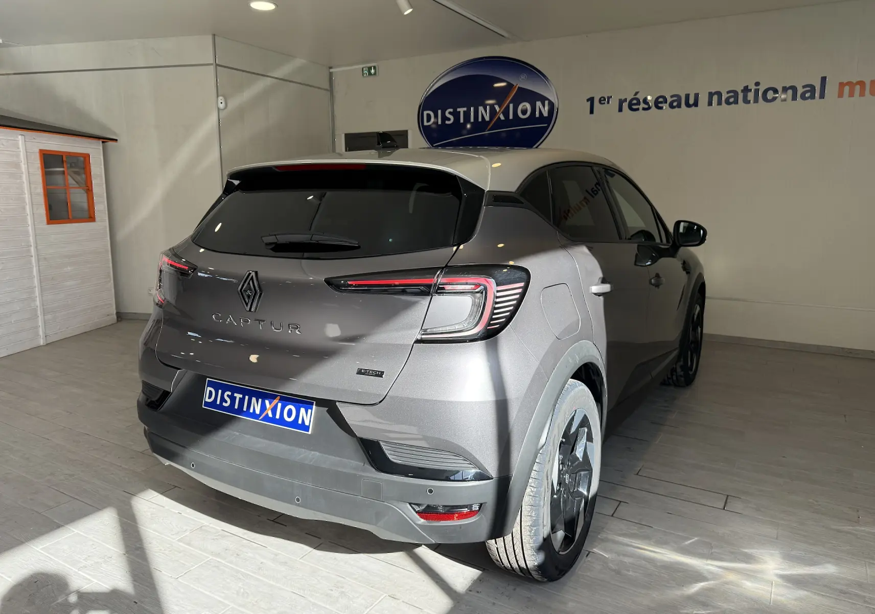 Vue 3/4 arrière droite d'un Renault Captur gris Cassiopée métal avec toit gris, feux arrière LED et jantes noires.