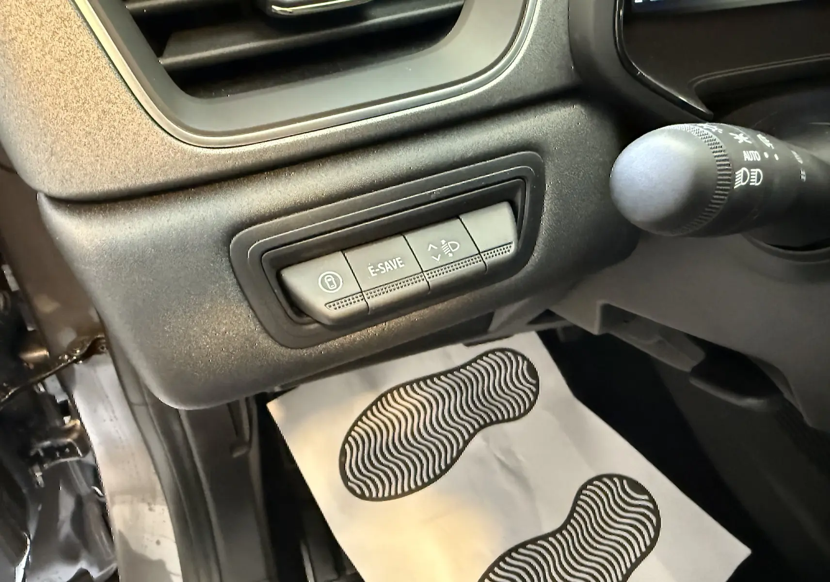 Gros plan sur les commandes E-SAVE et réglage des phares côté gauche du tableau de bord du Renault Captur gris 2025.