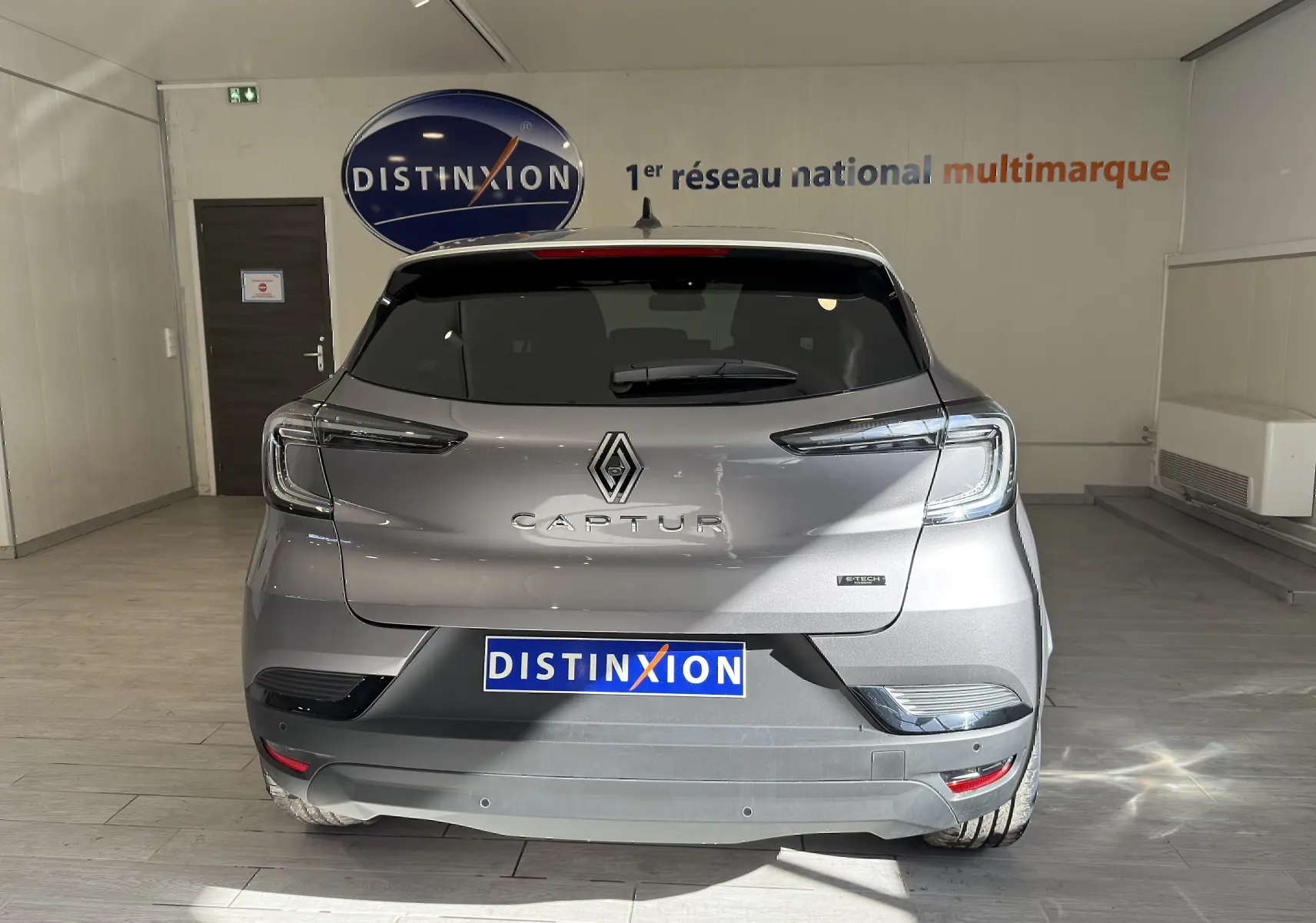 Vue arrière d'un Renault Captur gris Cassiopée métal avec toit gris, en intérieur showroom Distinxion.