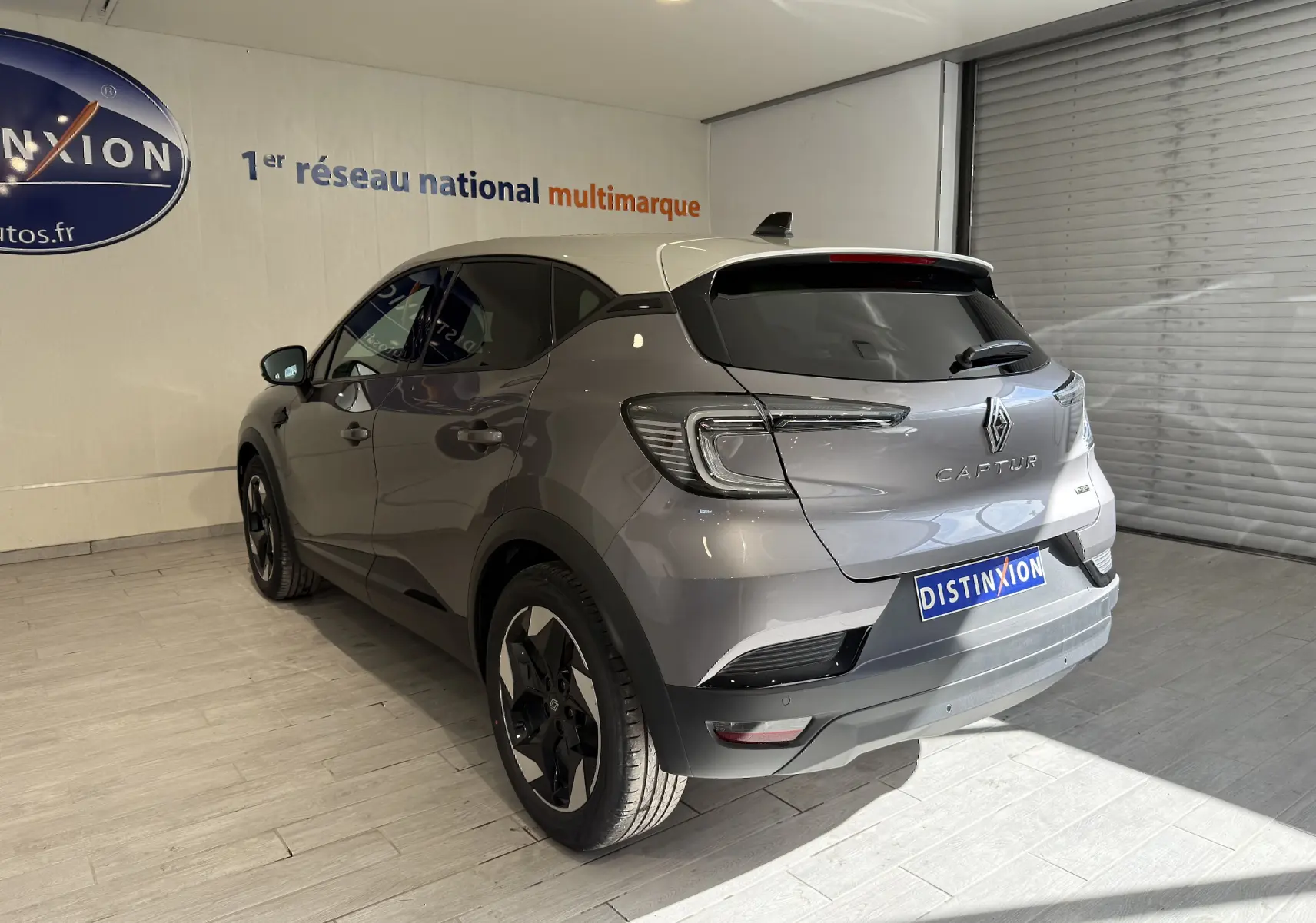 Vue 3/4 arrière gauche du Renault Captur gris Cassiopée métal avec toit gris et jantes noires en intérieur showroom.