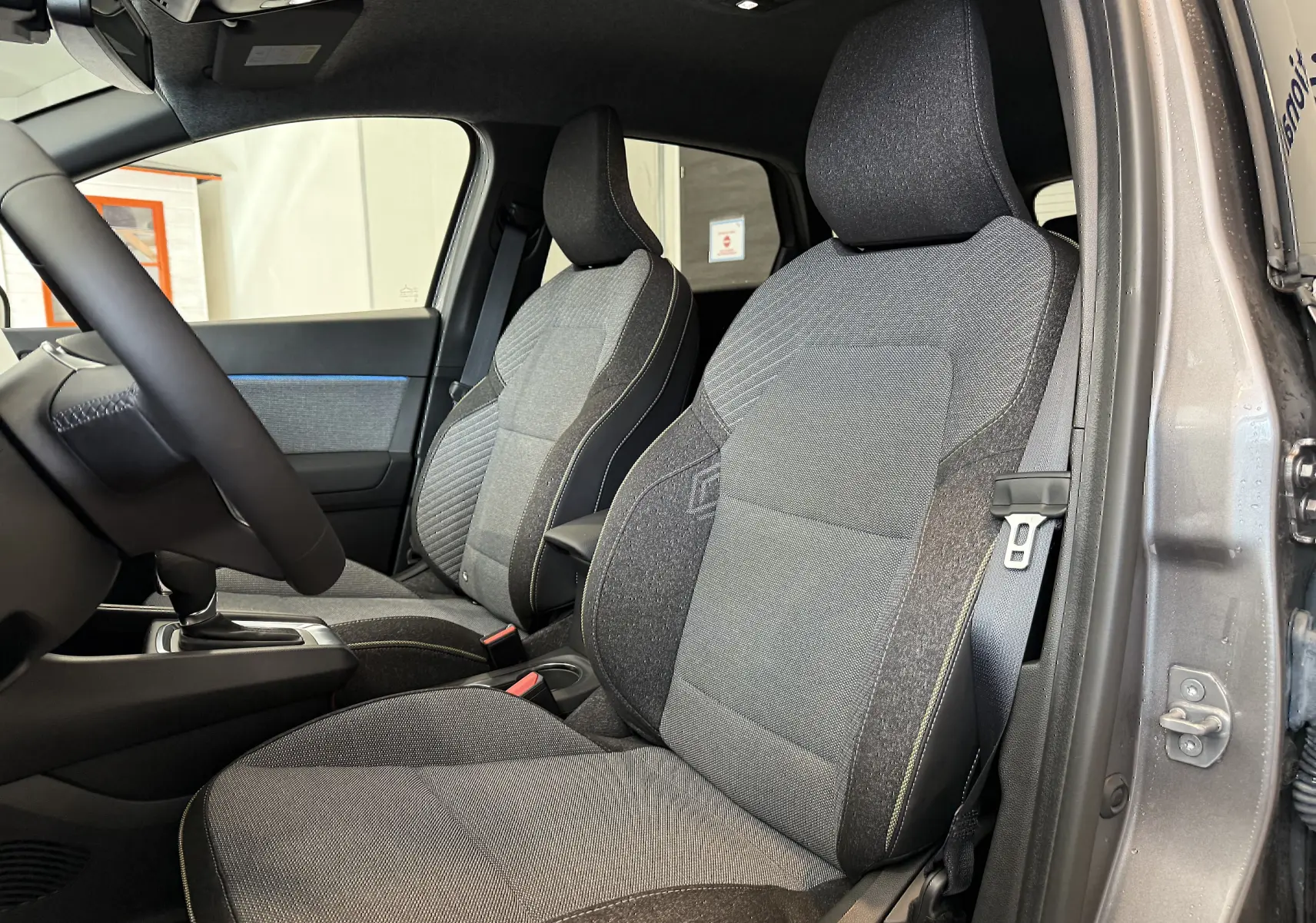 Vue intérieure côté conducteur du Renault Captur gris cassiopée, mettant en valeur les sièges tissu gris avec surpiqûres contrastées.