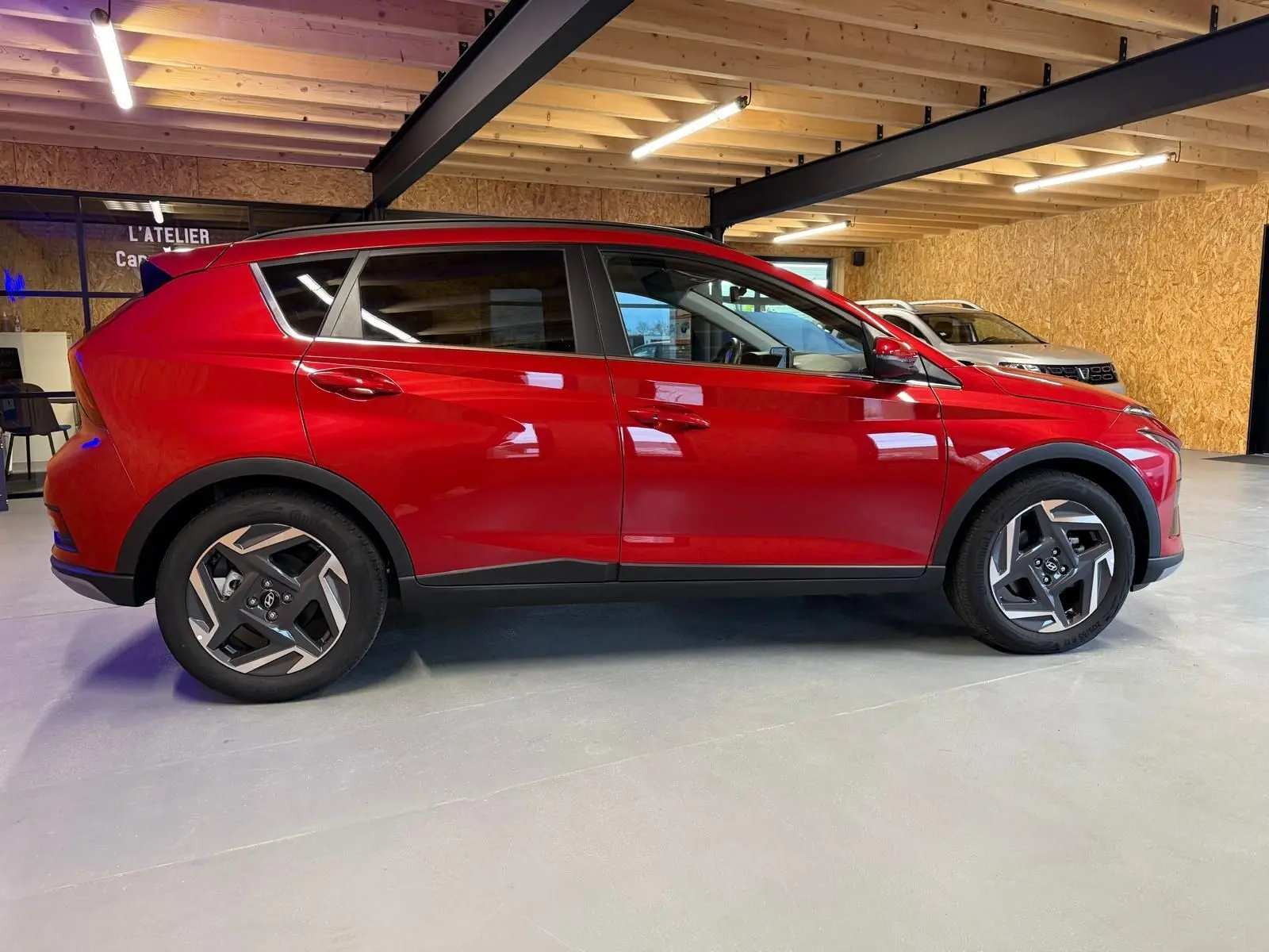 Profil droit d'un Hyundai Bayon rouge 2025 avec jantes alu 17'' et calandre noir laqué en intérieur d'atelier.