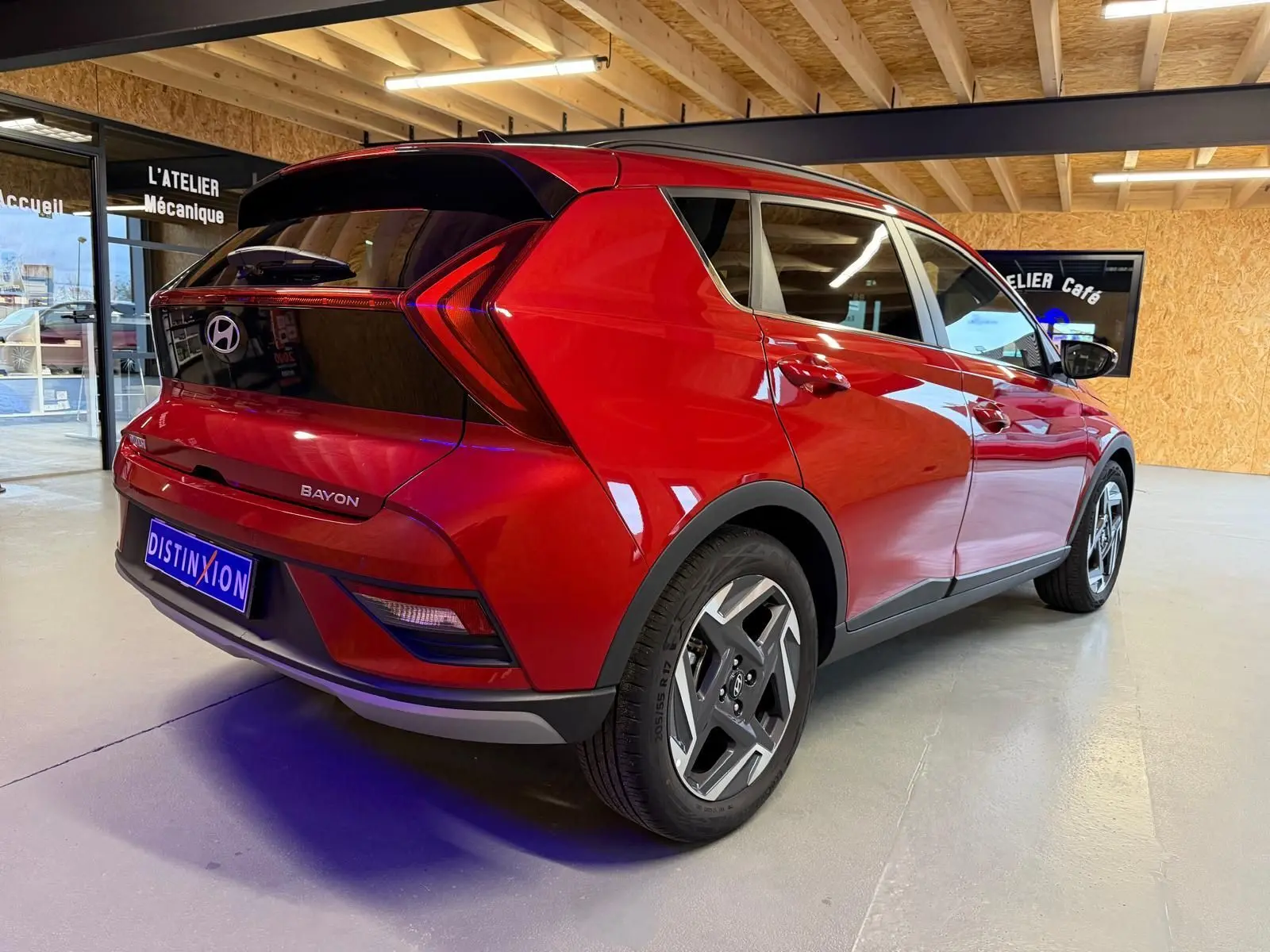 Vue 3/4 arrière droite du Hyundai Bayon rouge avec calandre noir laqué et jantes alu 17 pouces dans un showroom.