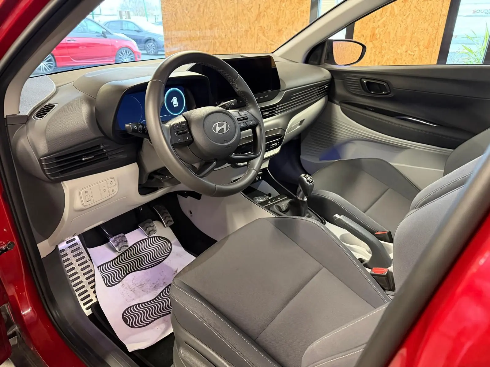 Vue intérieure côté conducteur de la Hyundai Bayon rouge 2025, avec tableau de bord moderne et volant cuir multifonctions.