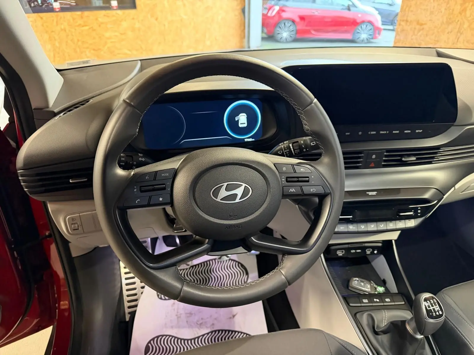 Vue intérieure centrée sur le volant cuir multifonctions et tableau de bord numérique du Hyundai Bayon rouge 2025.