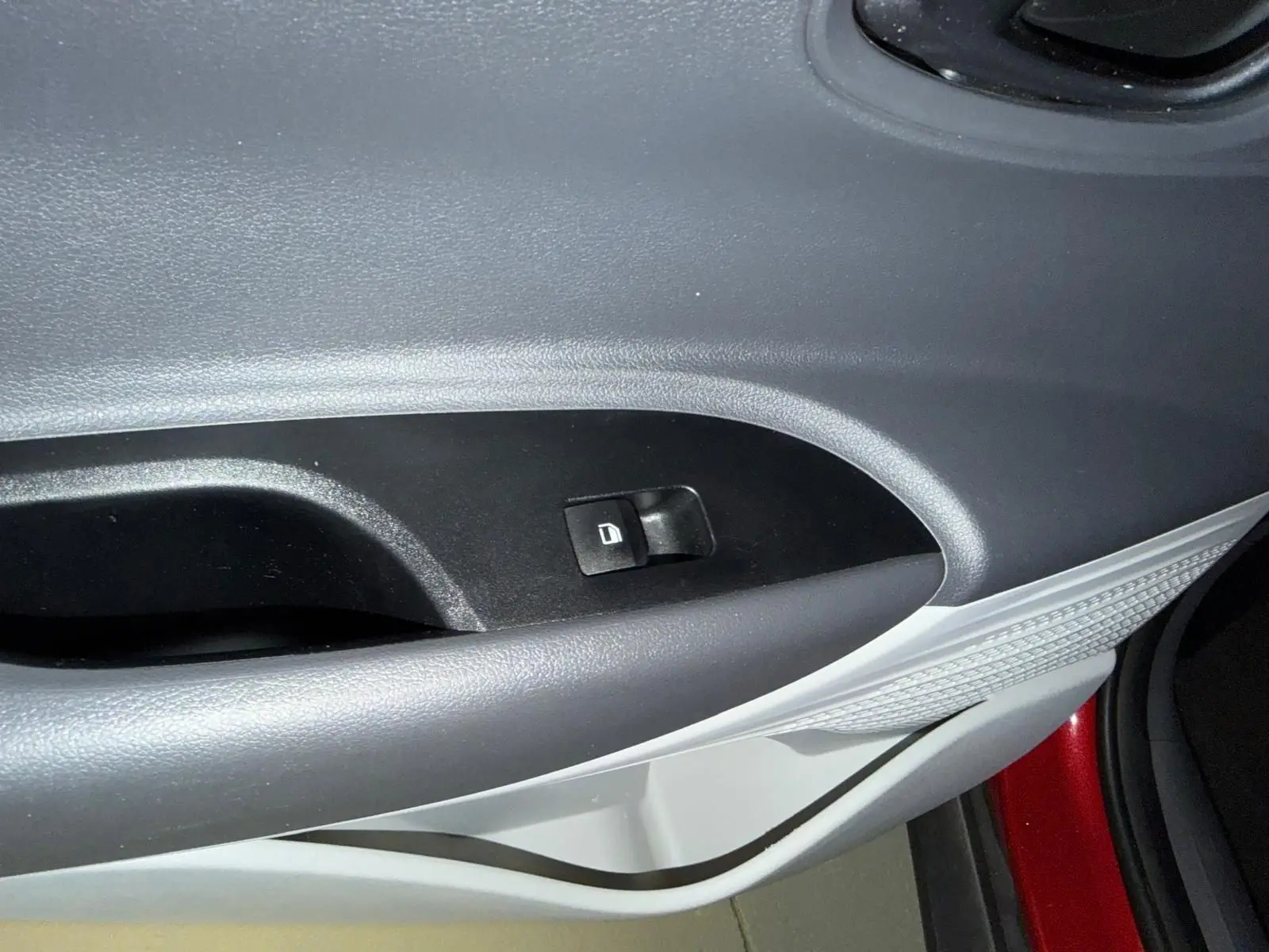 Gros plan sur la commande de verrouillage de porte côté gauche dans l'habitacle bi-ton noir et gris clair du Hyundai Bayon rouge.