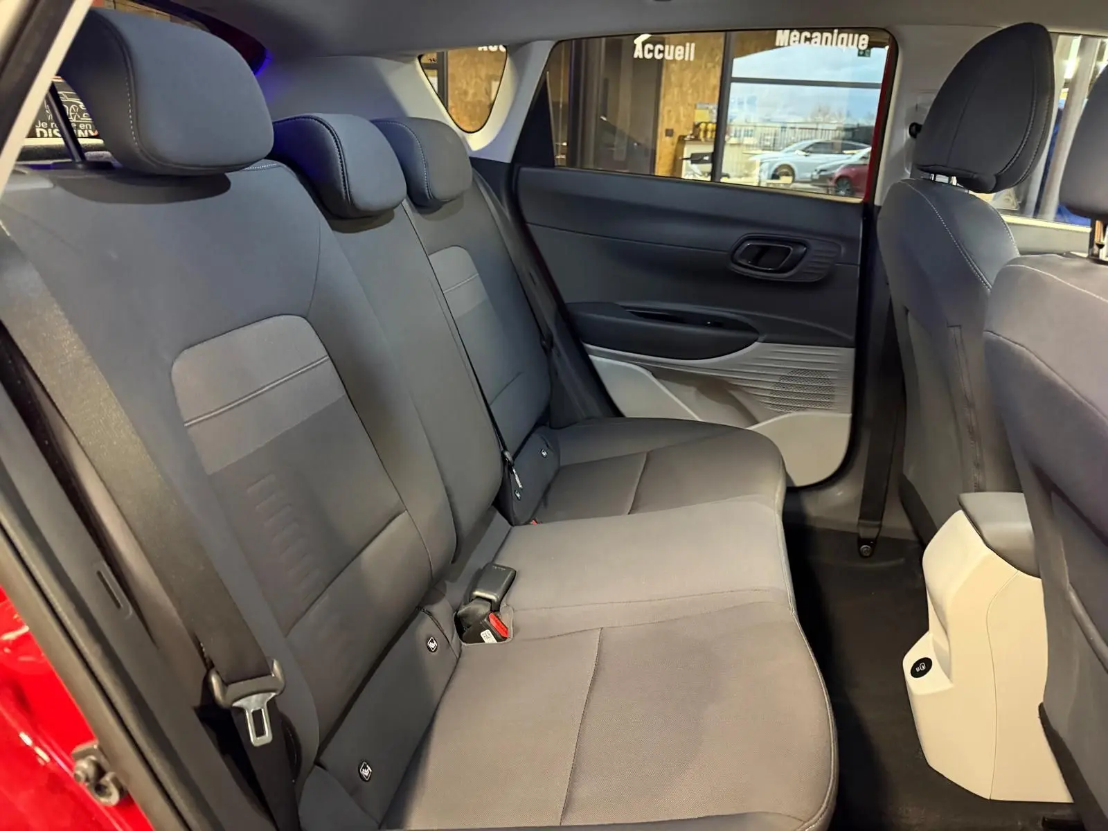 Vue intérieure arrière côté gauche du Hyundai Bayon rouge 2025, montrant la banquette grise et les portes ouvertes.