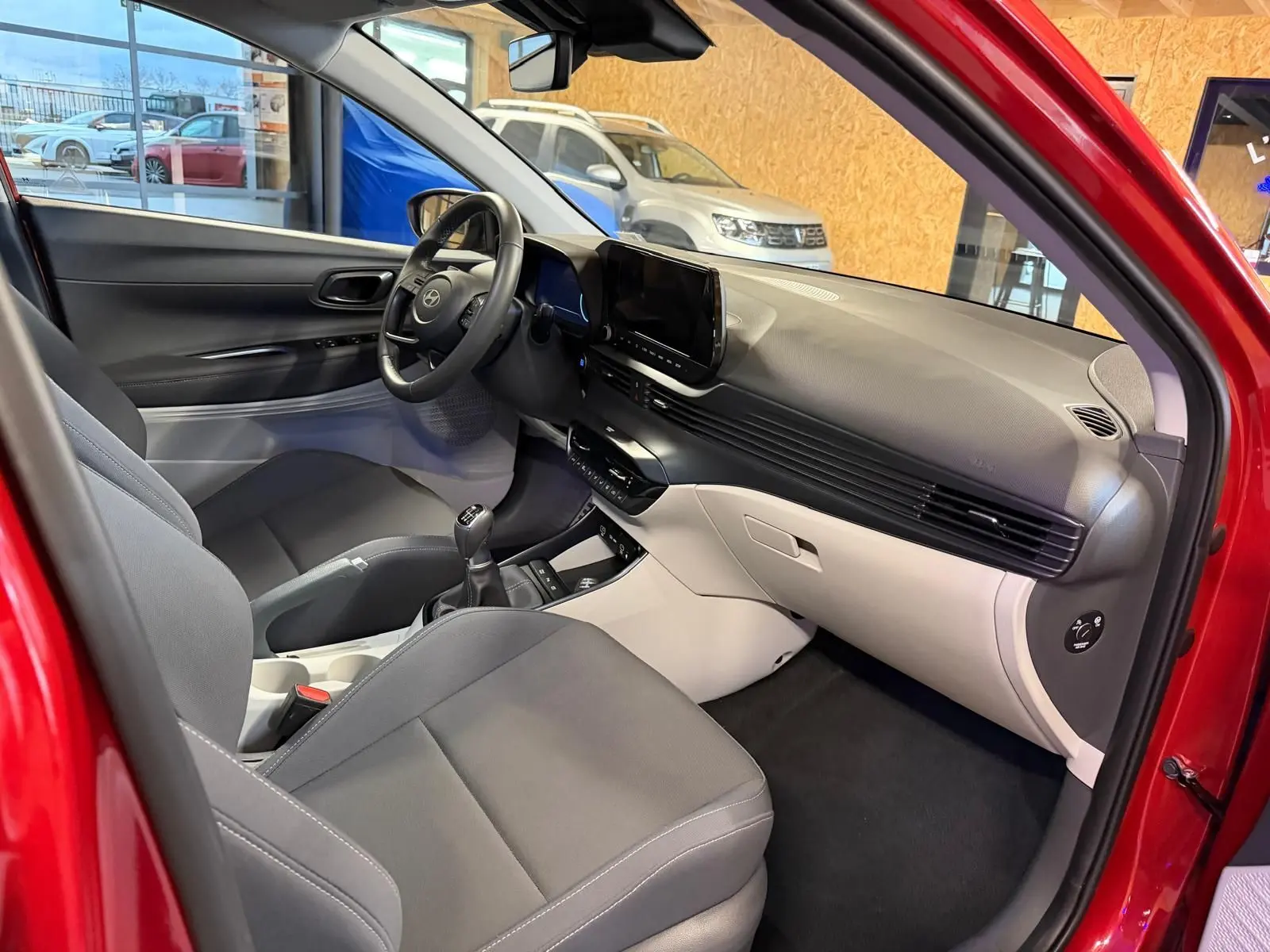 Intérieur bi-ton noir et gris clair du Hyundai Bayon rouge, vue côté passager avant avec tableau de bord moderne et écran tactile.