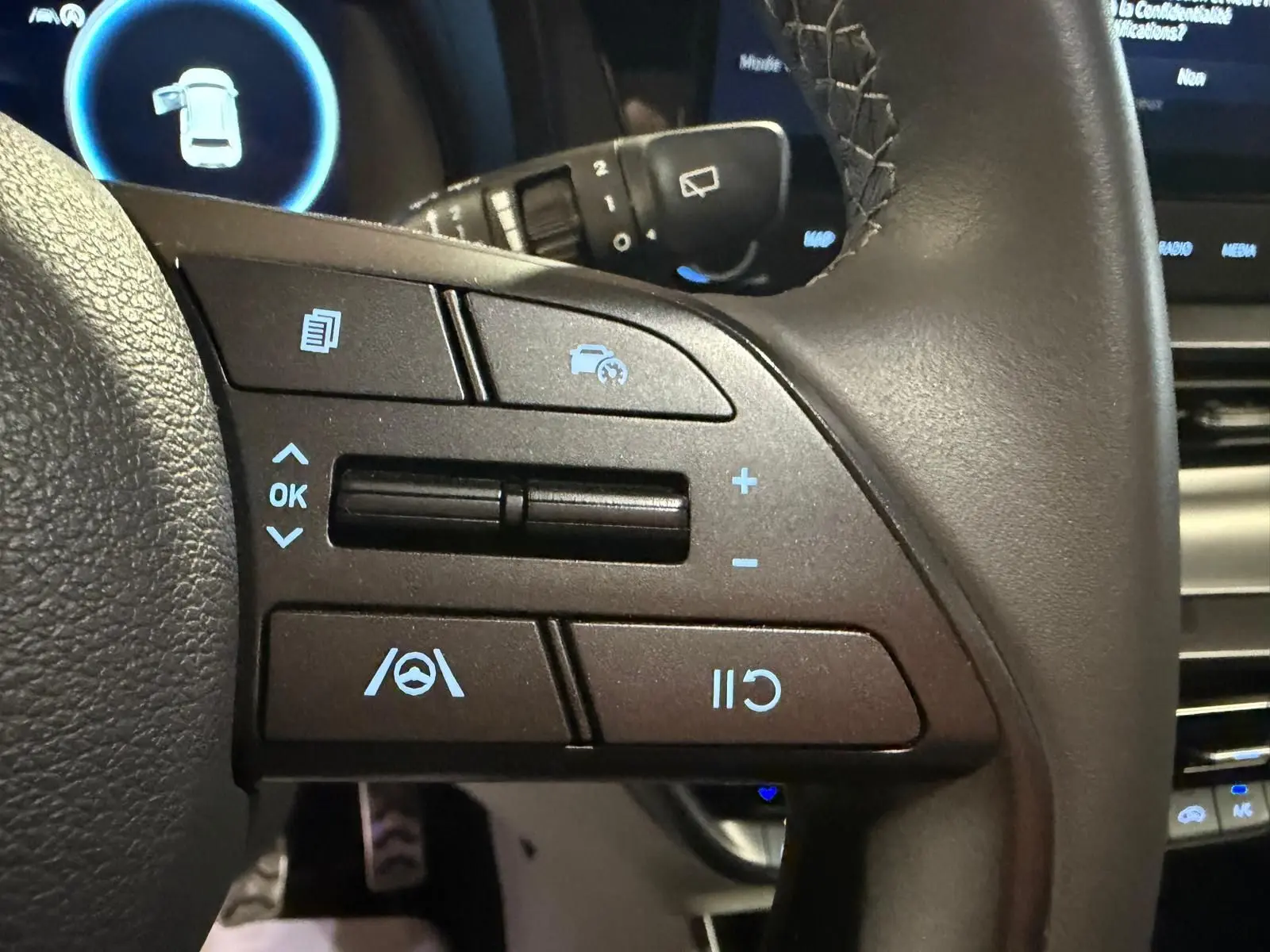 Gros plan sur les commandes multifonctions du volant cuir noir du Hyundai Bayon 2025, avec affichage numérique en arrière-plan.