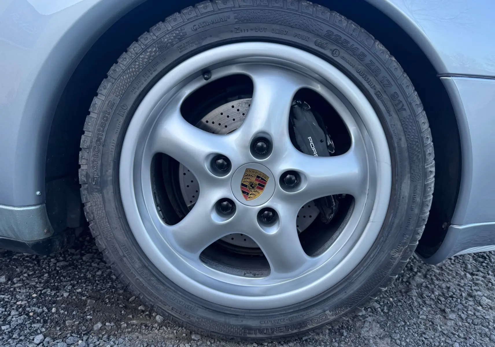 Gros plan sur la roue avant droite d'une Porsche 911 Carrera 2 gris polaire de 1996, avec passage de roue arrondi.