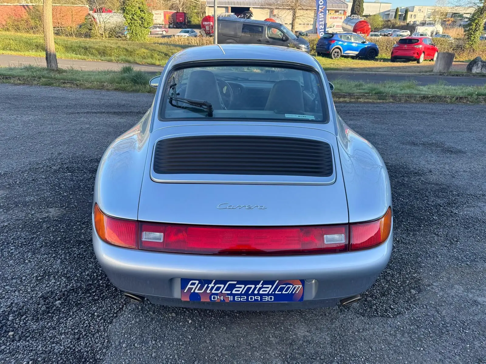 Vue arrière d'une Porsche 911 Carrera 993 gris polaire avec feu arrière continu et essuie-glace arrière visible.