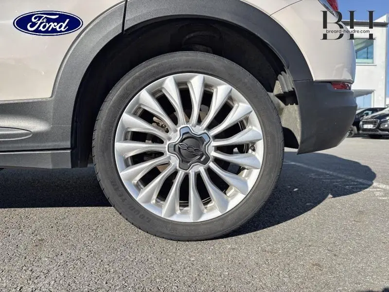 Gros plan sur la roue arrière droite argentée d'un FIAT 500X 2015 avec jante alu au design étoilé.