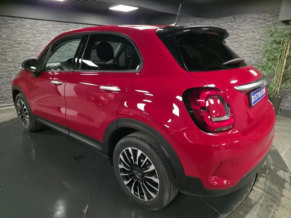 Vue 3/4 arrière droite d'un Fiat 500X rouge avec jantes alliage 17 pouces et vitres surteintées dans un intérieur gris.