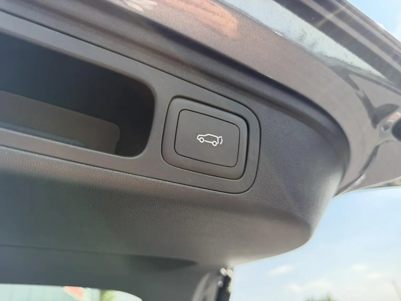Bouton d'ouverture électrique du hayon sur la partie intérieure du coffre d'un MG Motor EHS gris.