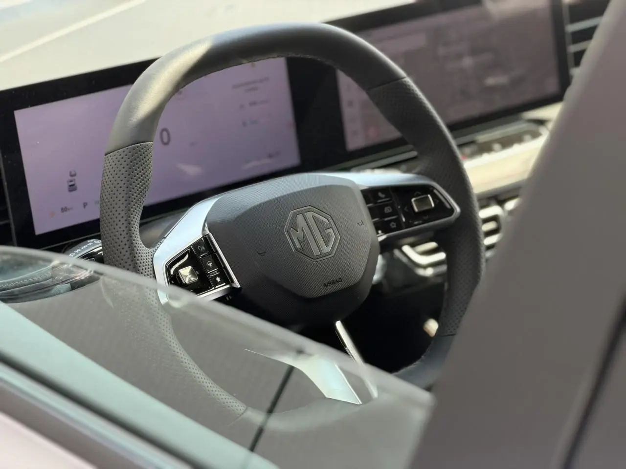 Vue rapprochée du volant noir perforé MG EHS 1.5 Hybrid+ 224 Luxury avec tableau de bord numérique en arrière-plan.