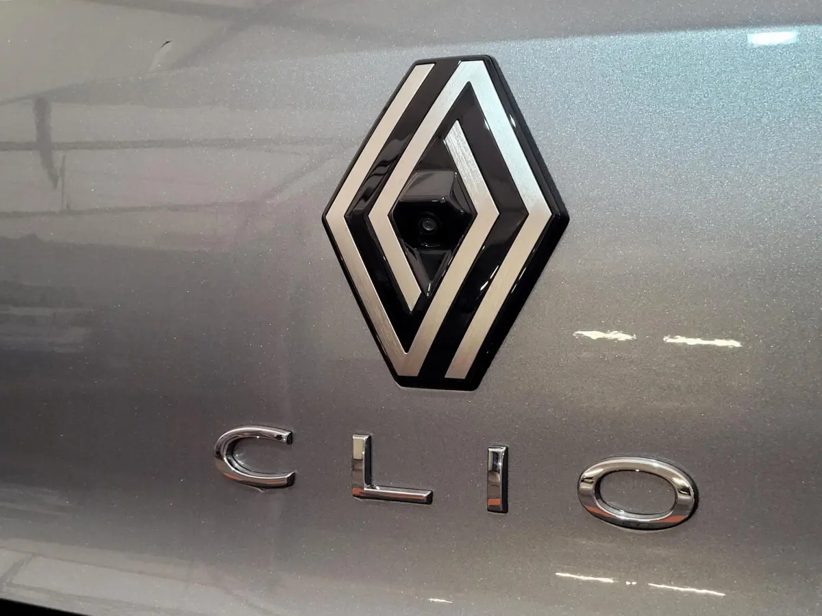 Gros plan sur le logo Renault et le nom Clio en lettres chromées sur la malle arrière gris foncé métallisé.