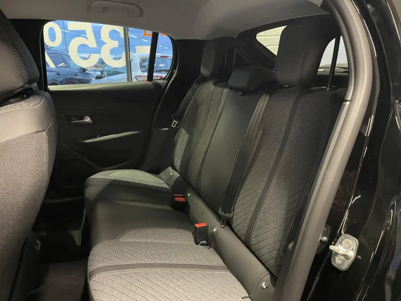 Vue intérieure de la banquette arrière d’une Peugeot 208 noire métallisée, avec sellerie tissu et ceintures de sécurité visibles.