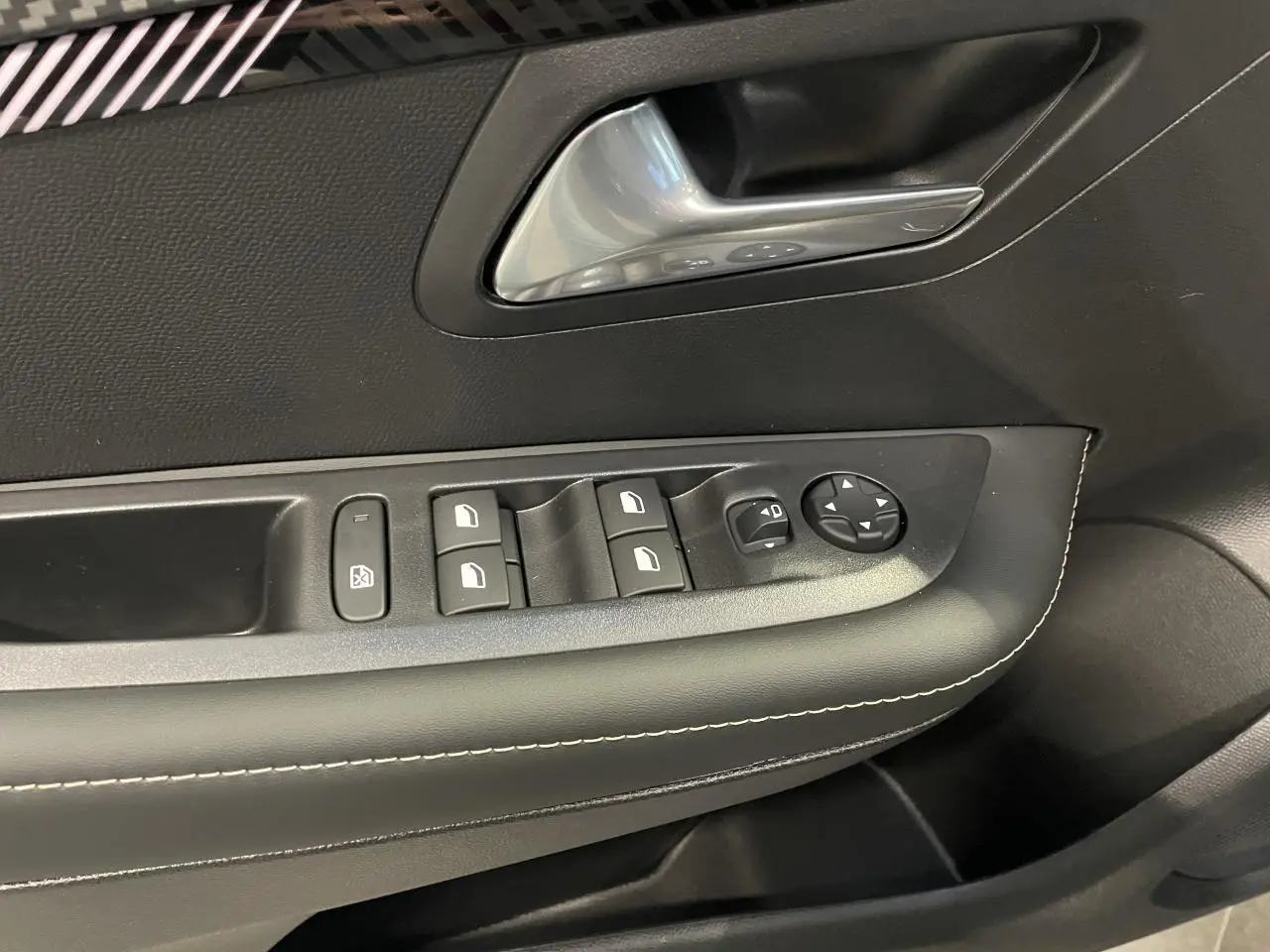 Détail de la commande des vitres et rétroviseurs côté gauche intérieur d'une Peugeot 208 noire métallisée.