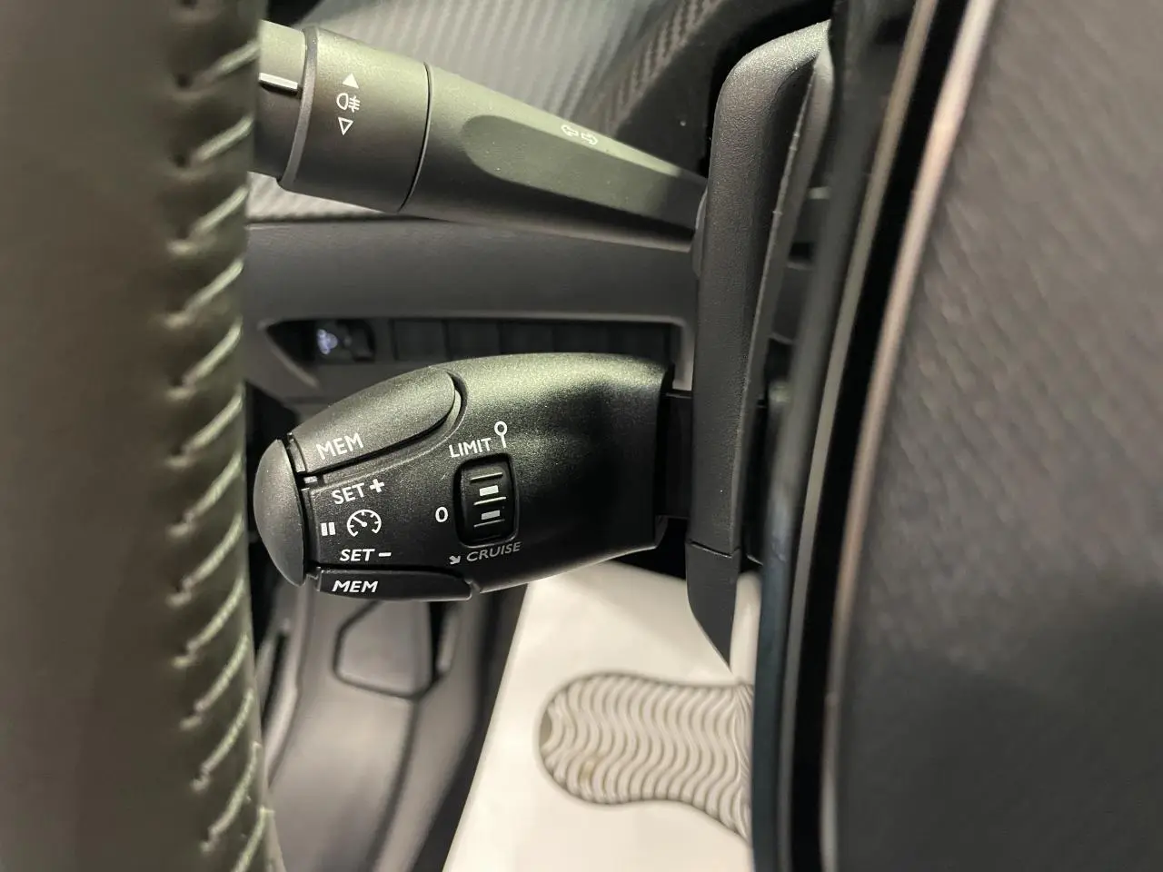 Gros plan sur la commande de régulateur de vitesse noire à gauche du volant dans l’habitacle d’une Peugeot 208 noire.