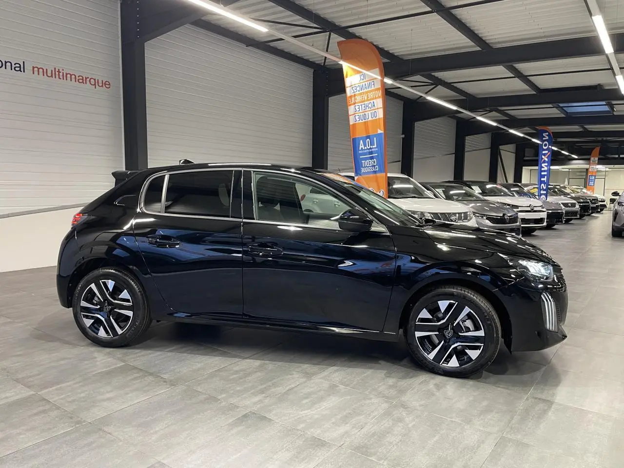 Peugeot 208 hybride noir métallisé vue de profil droit en intérieur avec jantes alliage bi-tons et vitres surteintées.