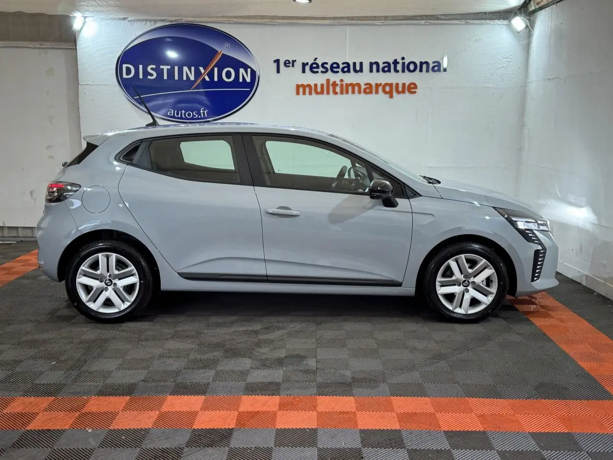 Profil droit d’une Renault Clio gris clair 2025 Evolution Blue dCi 100, stationnée en intérieur sur sol gris et orange.