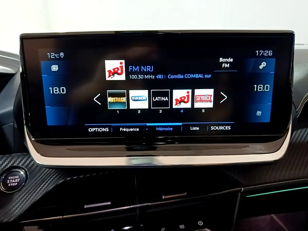 Écran tactile central du tableau de bord du Peugeot 2008 bleu, affichant les stations radio FM avec interface moderne.