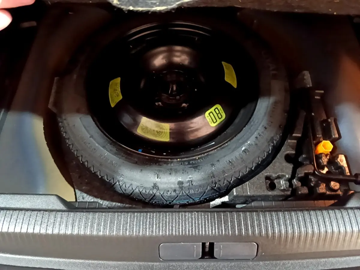 Vue plongeante sur la roue de secours noire et les outils de bord dans le coffre d’un Peugeot 2008 bleu.