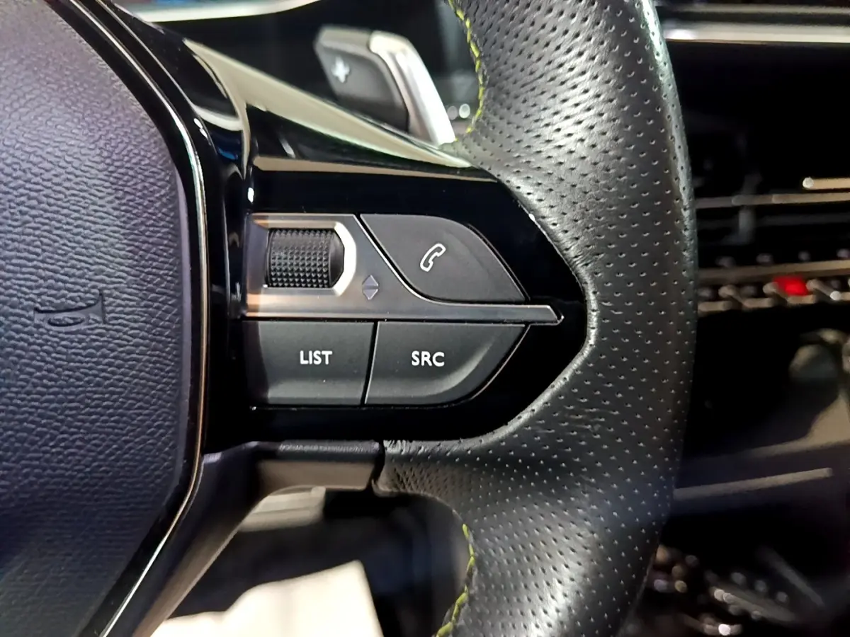 Gros plan sur les commandes gauche du volant cuir perforé du Peugeot 2008 Bleu, avec boutons LIST et SRC visibles.