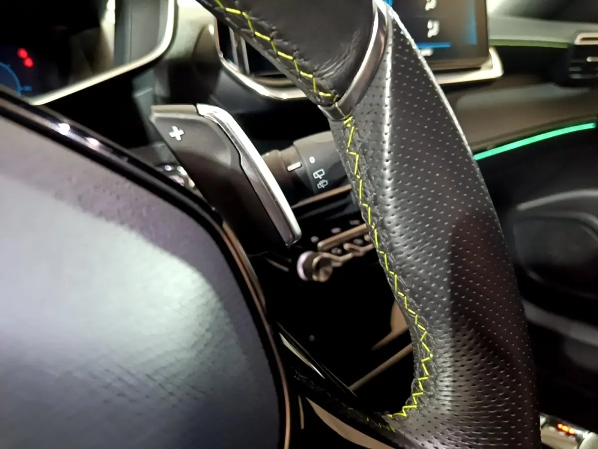 Gros plan sur le volant cuir noir avec surpiqûres jaunes et palettes de changement de vitesse dans l’habitacle du Peugeot 2008 bleu.