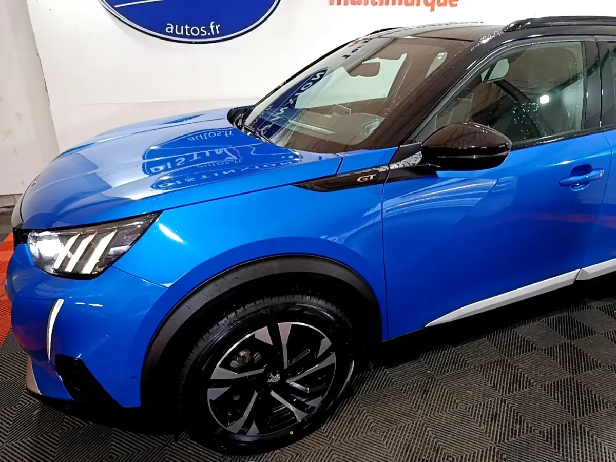 Vue 3/4 avant gauche d’un Peugeot 2008 GT bleu avec jantes noires et toit noir brillant.
